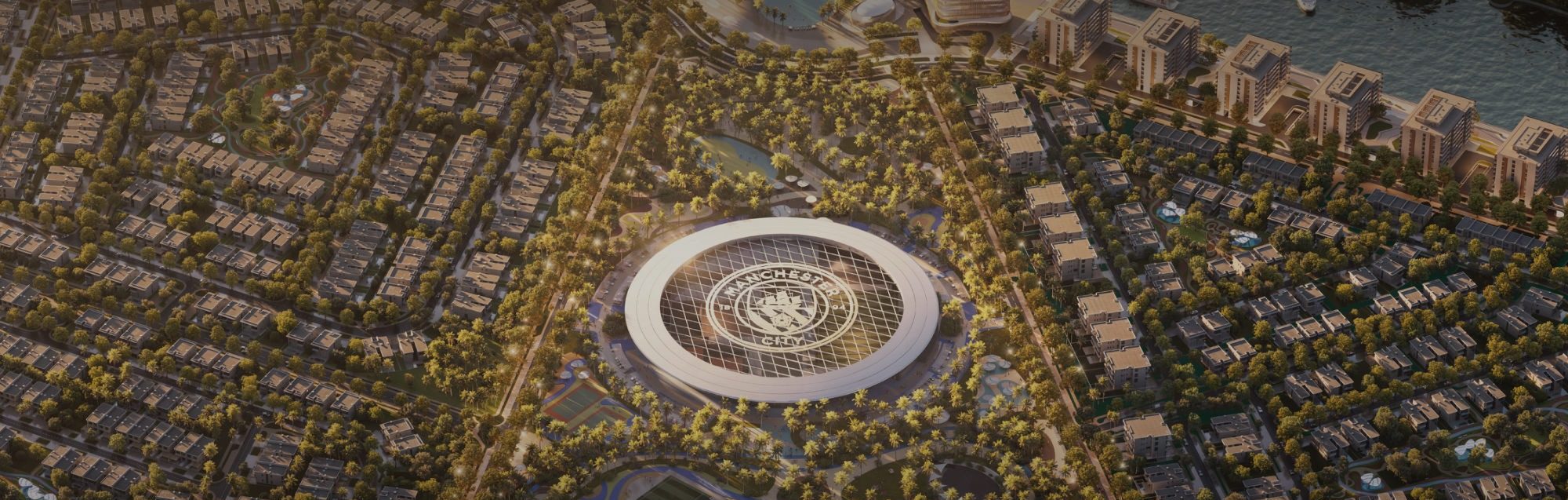 Aerial render of Manchester City Yas Residences at dusk: villa streets around a circular arena carrying the Manchester City crest, with apartment buildings along the canal