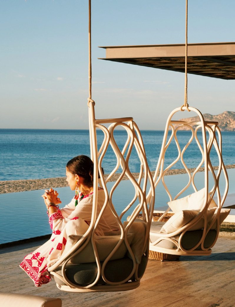 A child in a hanging chair on a terrace overlooking the sea
